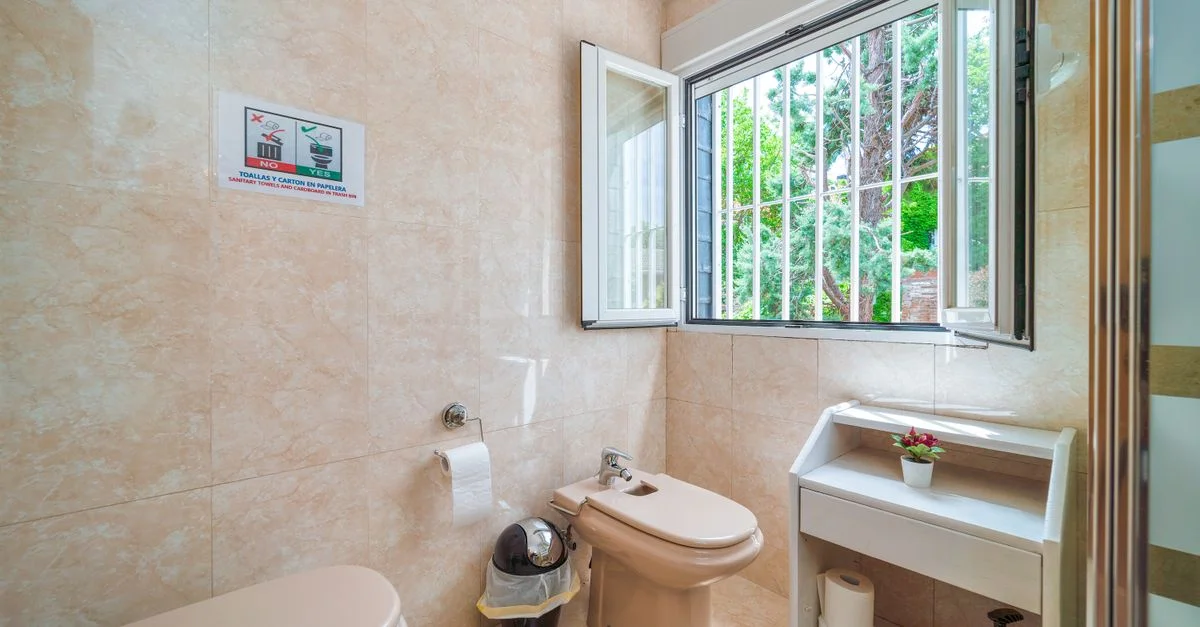 Intérieur moderne de salle de bain avec un bidet, des toilettes et une fenêtre ouverte offrant une vue extérieure.