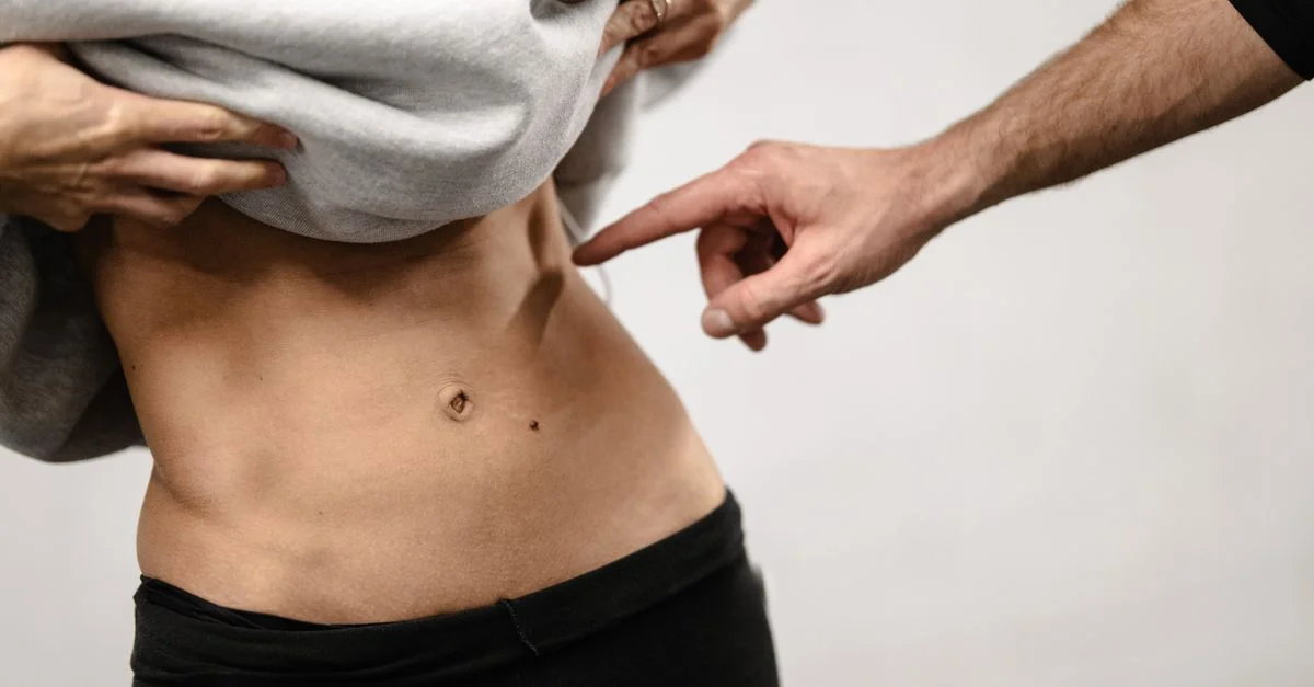 Gros plan intime de la zone abdominale tonique d'une personne avec une main pointant, soulignant la forme physique.