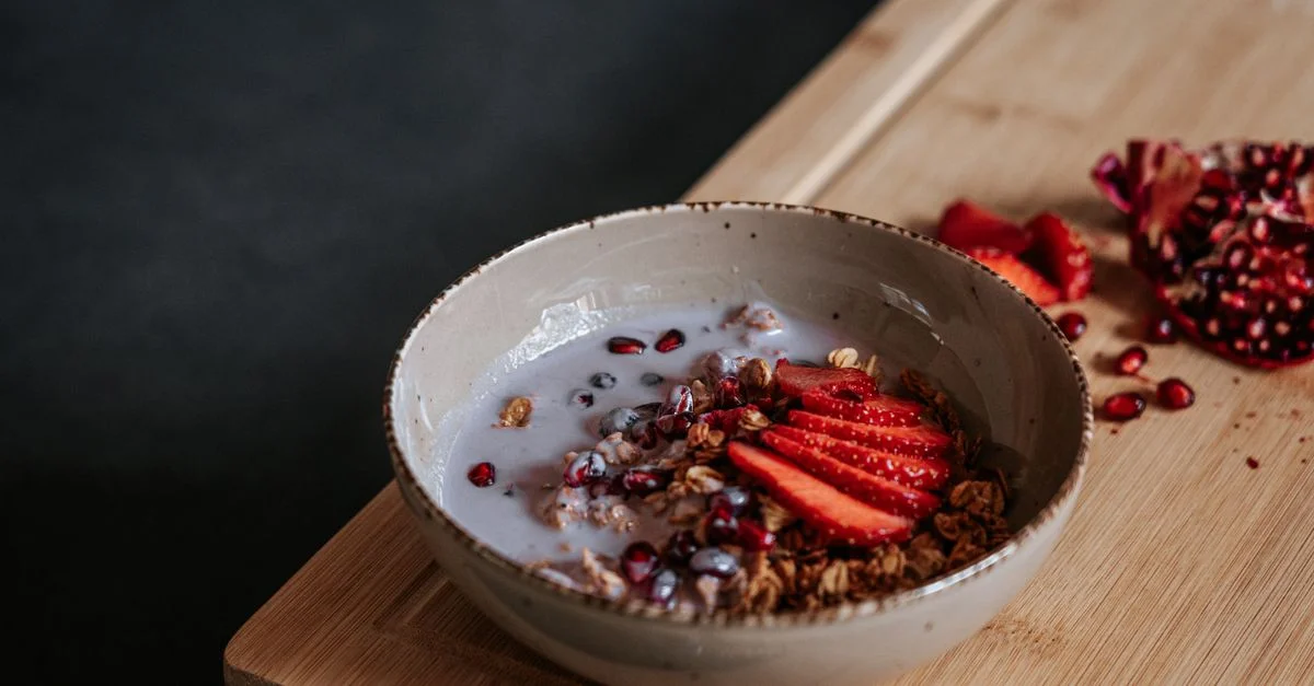 Un bol de petit-déjeuner sain avec du granola, des fraises tranchées et des graines de grenade dans du lait.