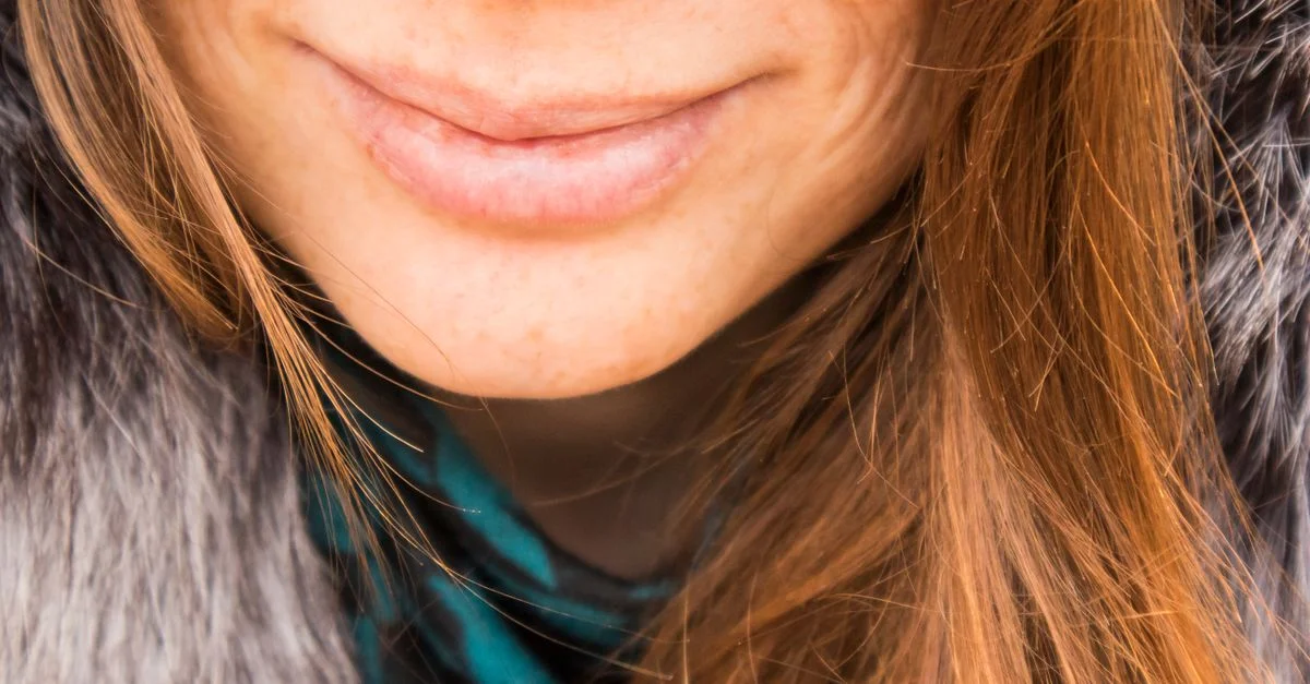 Gros plan sur le sourire d'une femme, mettant en valeur ses cheveux roux naturels et ses vêtements d'hiver chauds.