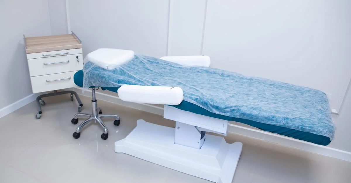 Salle d'examen médicale stérile et moderne avec lit ajustable et cabinet.