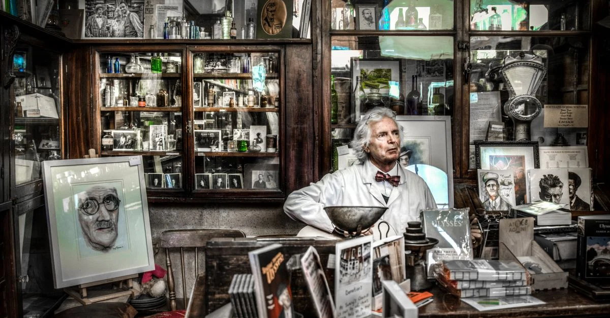 Une pharmacie vintage présentant des livres, des portraits et un pharmacien dans un cadre réfléchi.