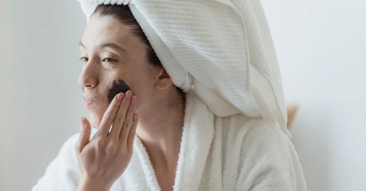 Une femme applique un masque facial dans le cadre de sa routine de soins de la peau du matin, enveloppée dans une serviette confortable.