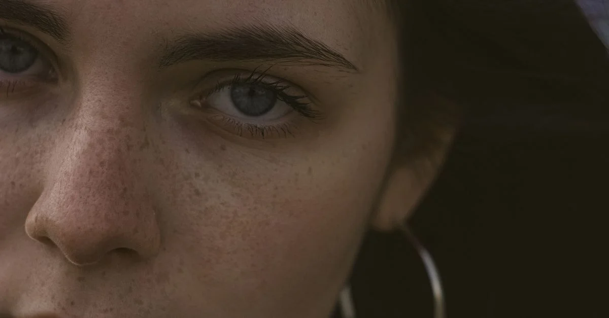 Gros plan intime sur le visage d'une femme mettant en valeur ses taches de rousseur et ses yeux.