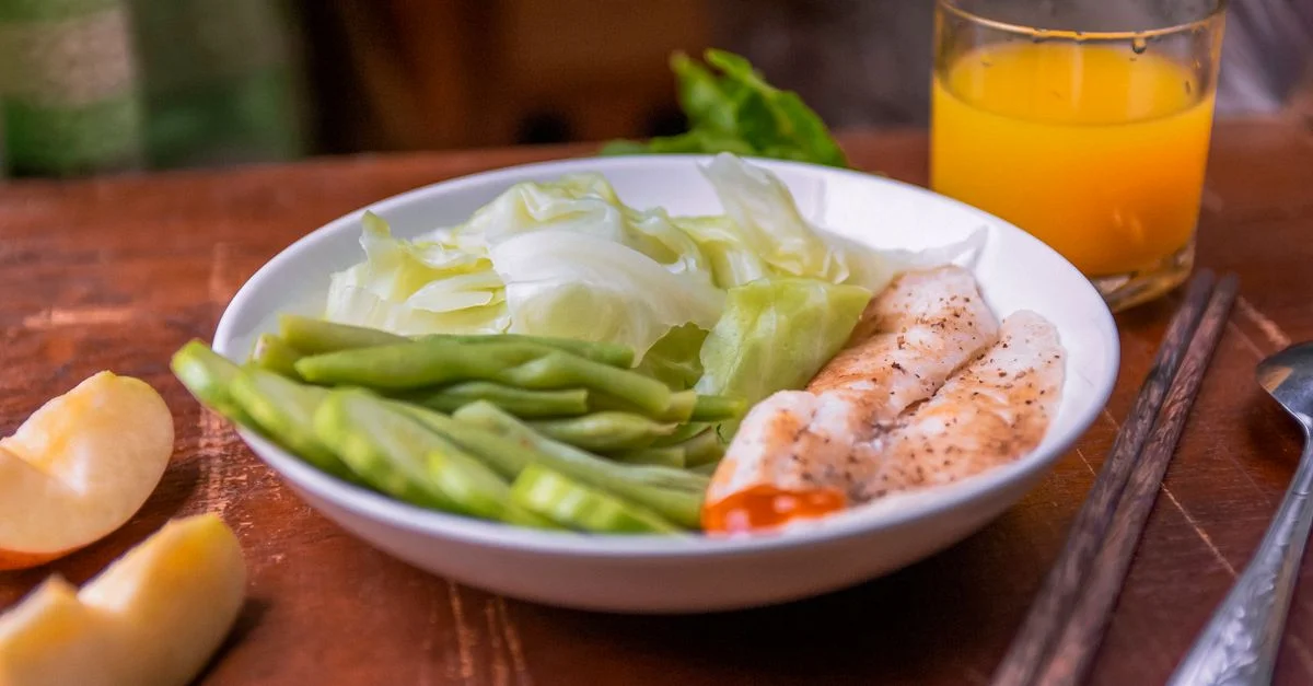 Repas sain avec du poisson, des haricots verts et du chou, accompagné d'un verre de jus d'orange.
