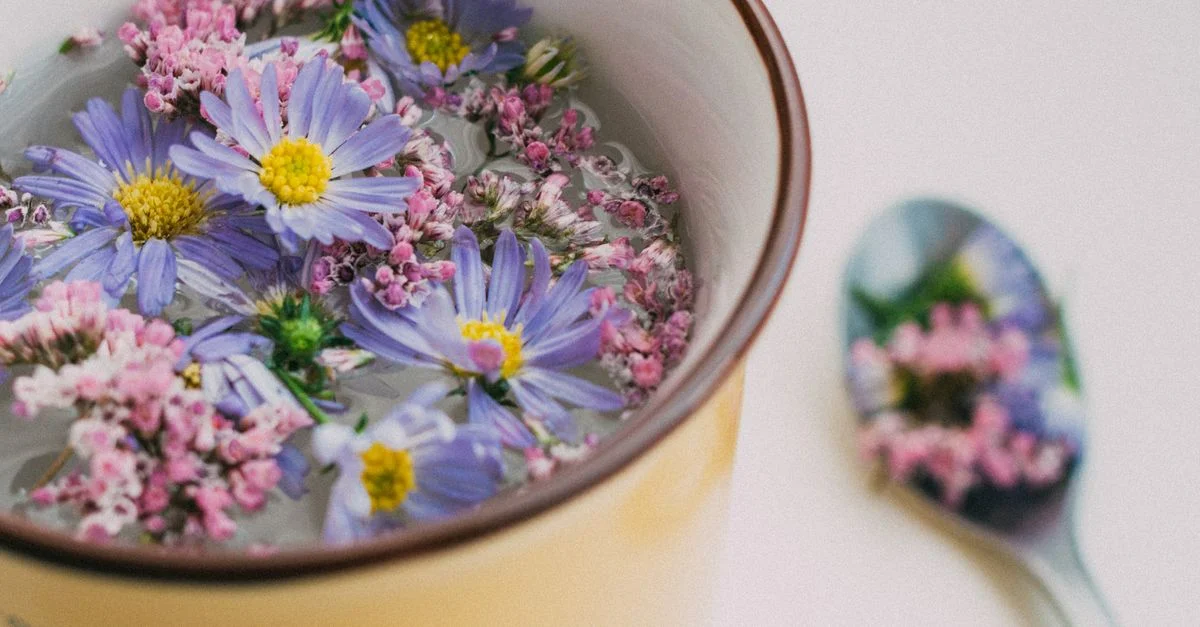 De délicates fleurs violettes et roses flottent dans une tasse, avec une cuillère reflétant des motifs floraux.