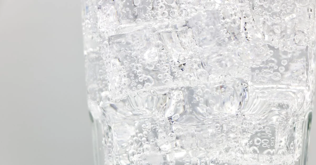 Eau pétillante rafraîchissante avec des glaçons dans un verre transparent, vue en gros plan.