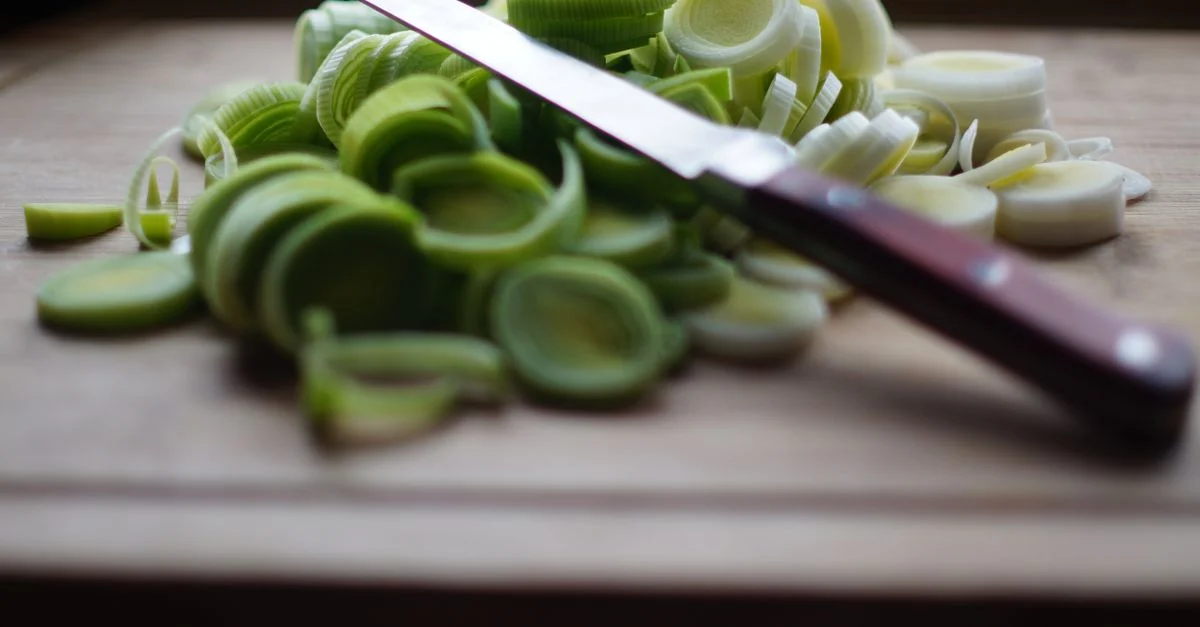 Poireaux fraîchement tranchés sur une planche à découper en bois avec un couteau aiguisé, idéal pour les thèmes de cuisine et de préparation alimentaire.