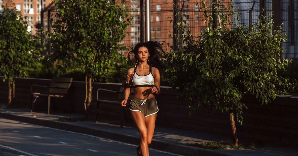 Femme en forme courant sur un trottoir de la ville pendant la journée, incarnant un mode de vie actif.