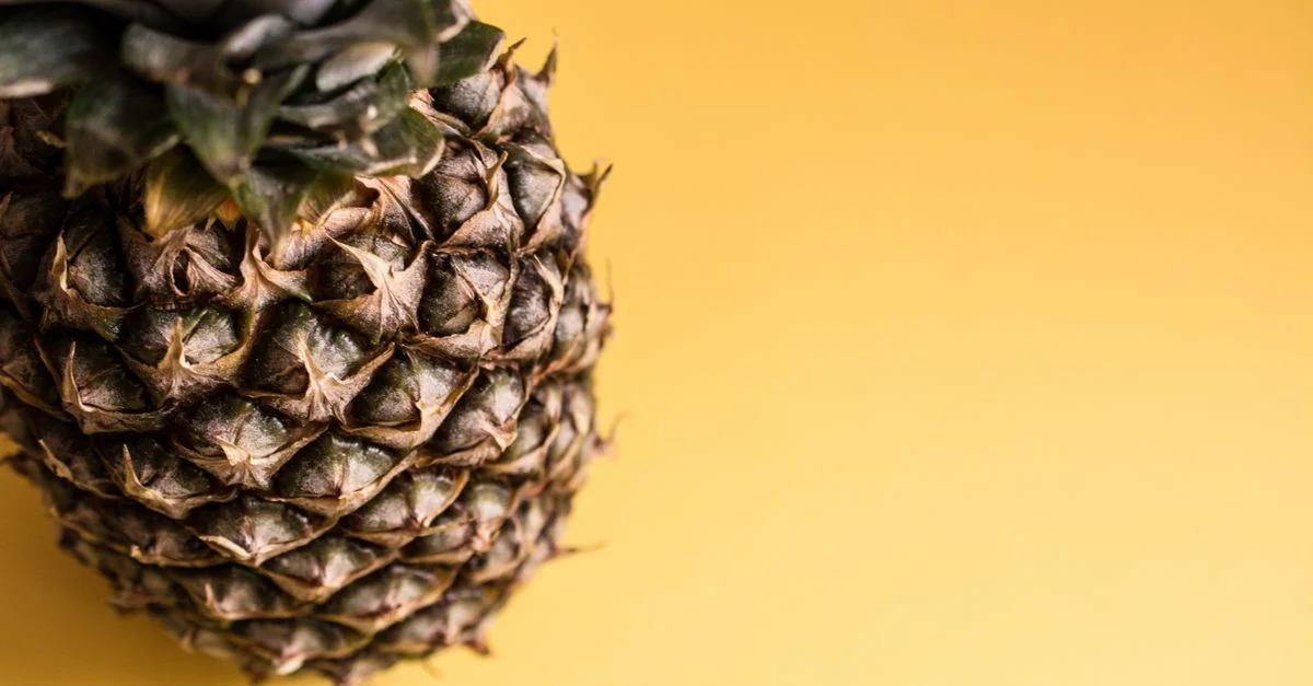 Gros plan sur un ananas frais sur un fond jaune vif, mettant en valeur sa texture.