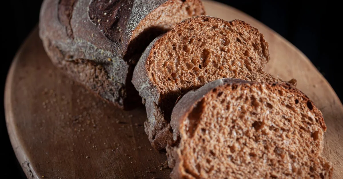 Gros plan de pain artisanal tranché sur une planche en bois rustique, mettant en valeur la texture et la croûte.