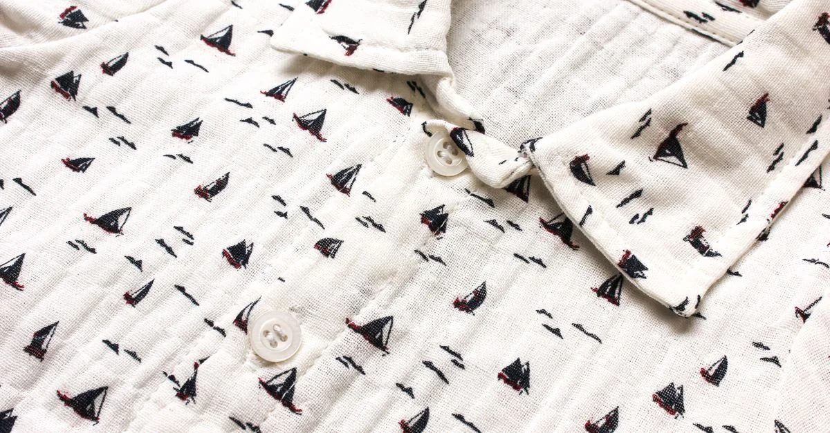 Gros plan d'une chemise blanche avec des motifs de voiliers sur du tissu en mousseline, comportant des boutons.