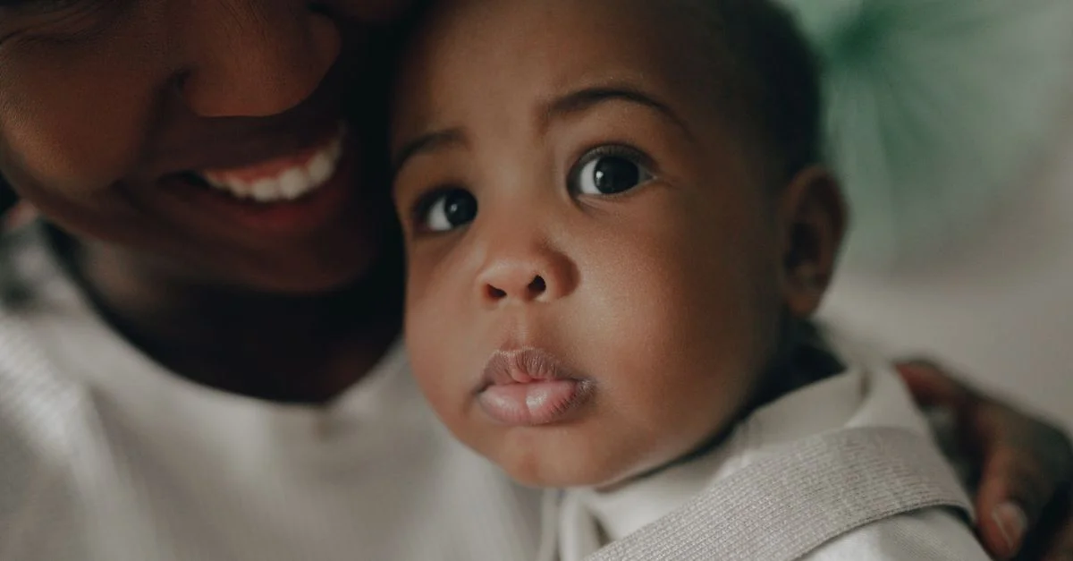 Une mère afro-américaine tient affectueusement son bébé, mettant en avant un gros plan de visages pleins de tendresse.