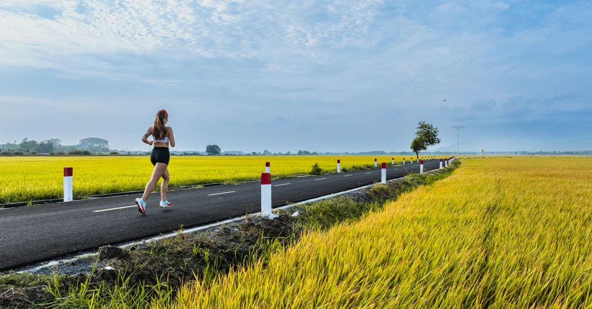 Une femme fait du jogging le long d'une route tranquille à travers des terres agricoles luxuriantes en été.