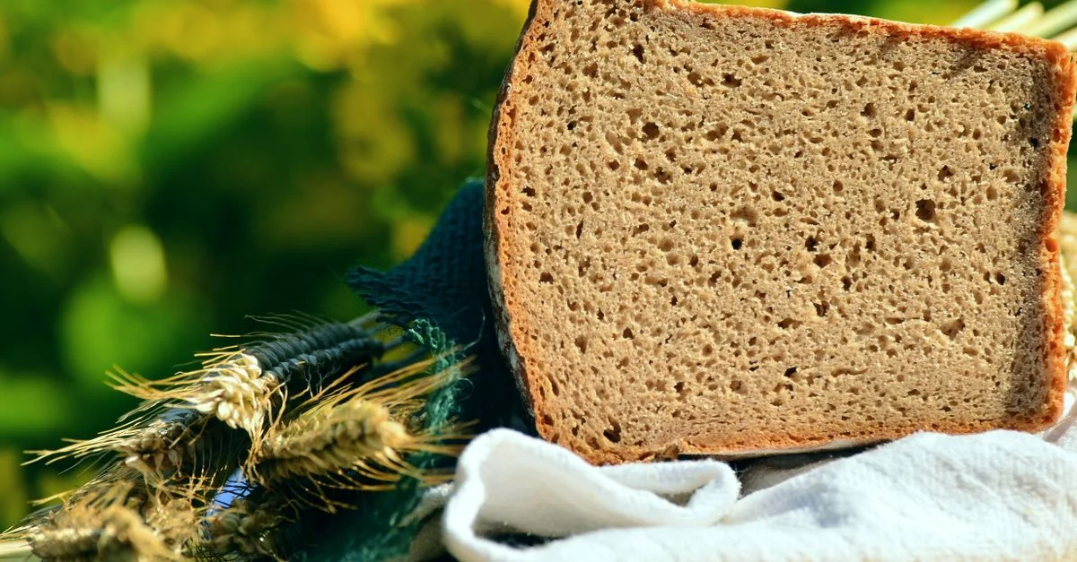 Gros plan sur une tranche de pain de seigle rustique avec des tiges de blé par une journée ensoleillée.