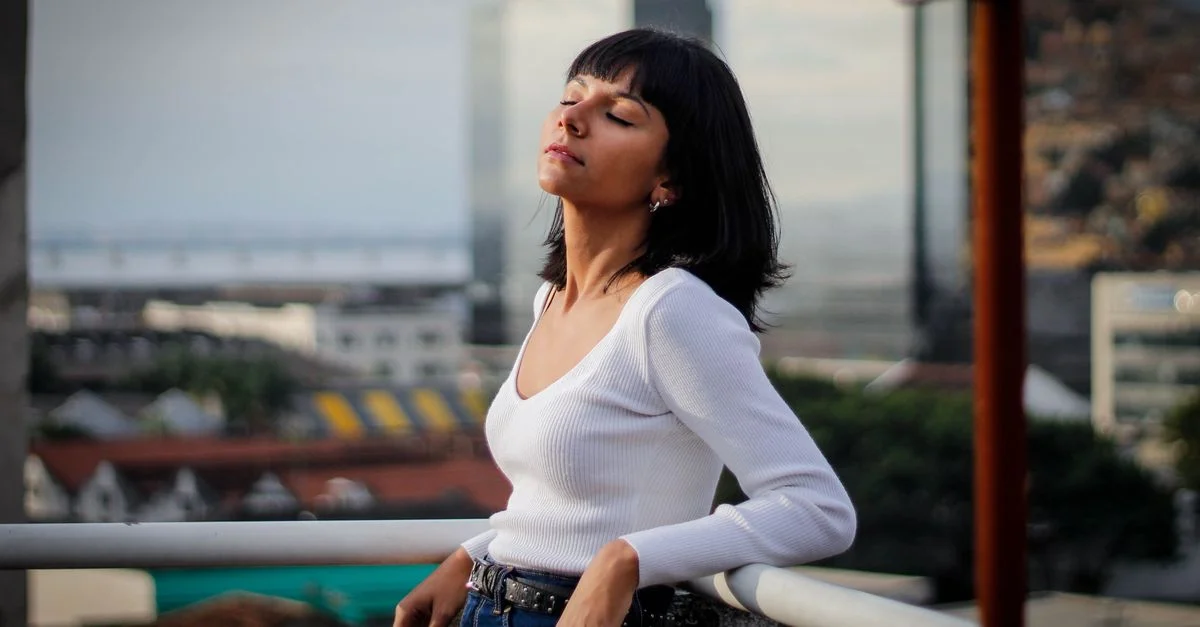 Une femme à la mode profite de l'extérieur en s'appuyant sur la balustrade d'un balcon dans un cadre urbain.