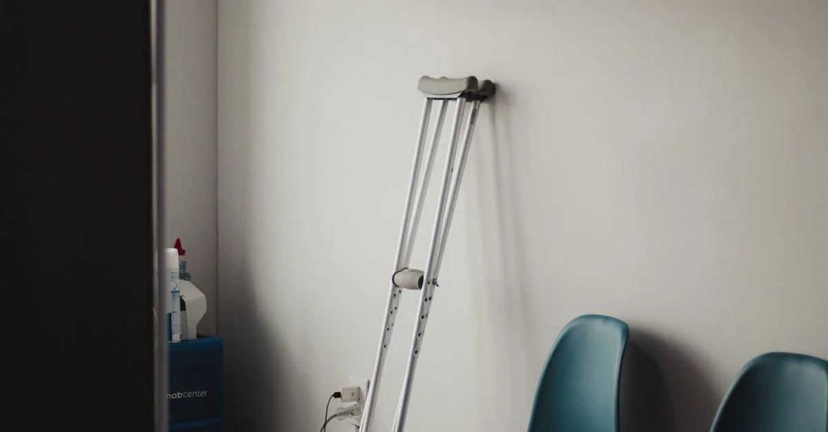 Béquilles reposant contre un mur dans une salle d'attente minimaliste avec des chaises bleues.