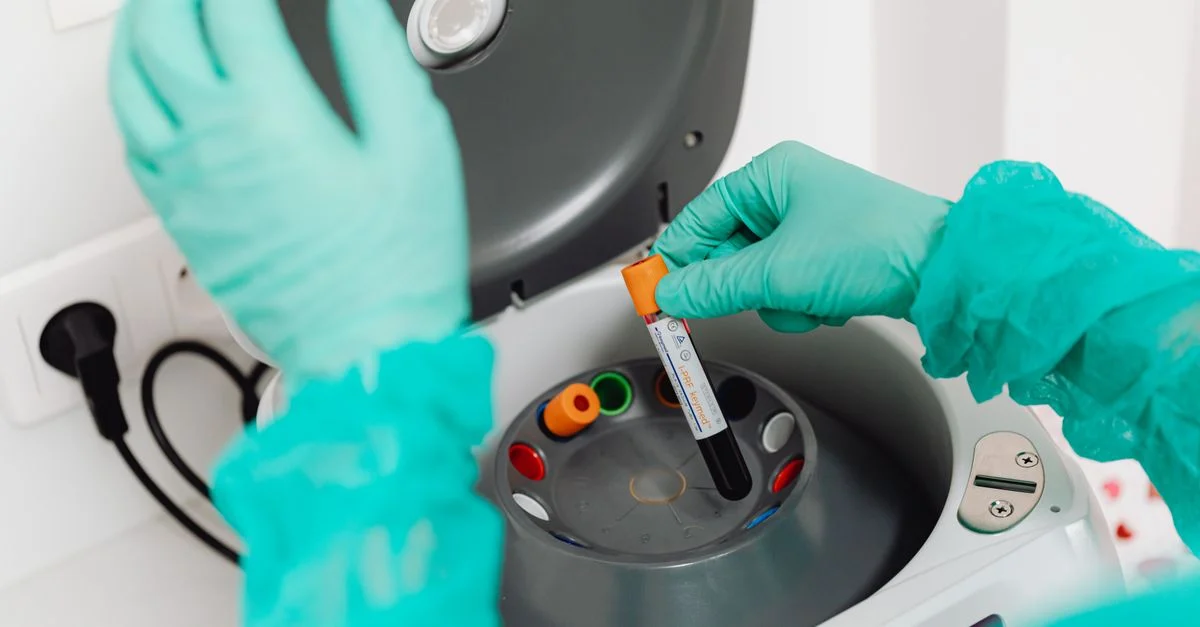 Un technicien de laboratoire portant des gants utilise une centrifugeuse pour l'analyse du sang dans un environnement de laboratoire moderne.