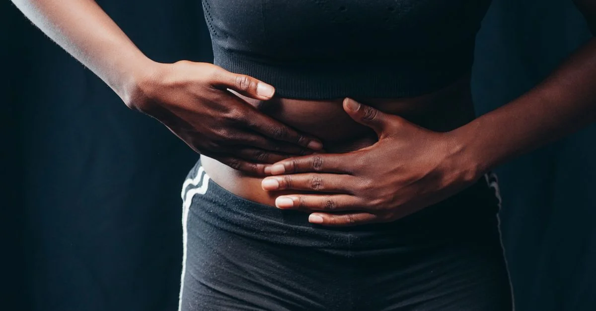 Gros plan d'une personne pressant les mains sur son abdomen, indiquant un inconfort ou une douleur, sur fond noir.
