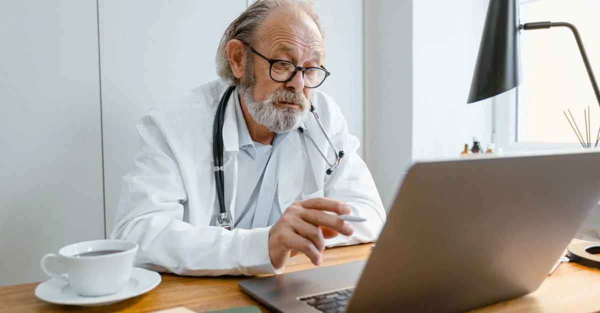 Médecin senior utilisant un ordinateur portable pour une consultation de télésanté dans un bureau.