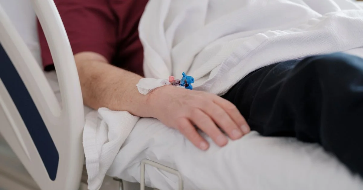 Gros plan sur la main d'un patient avec une perfusion allongé sur un lit d'hôpital.