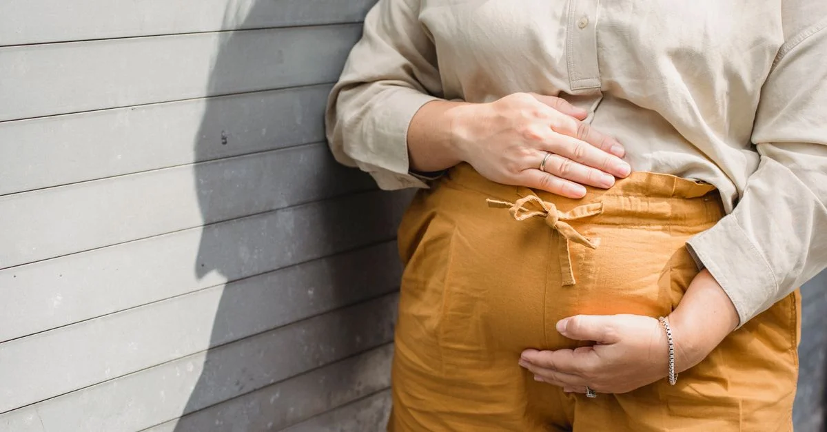 Gros plan d'une femme enceinte caressant son ventre contre un mur ensoleillé.