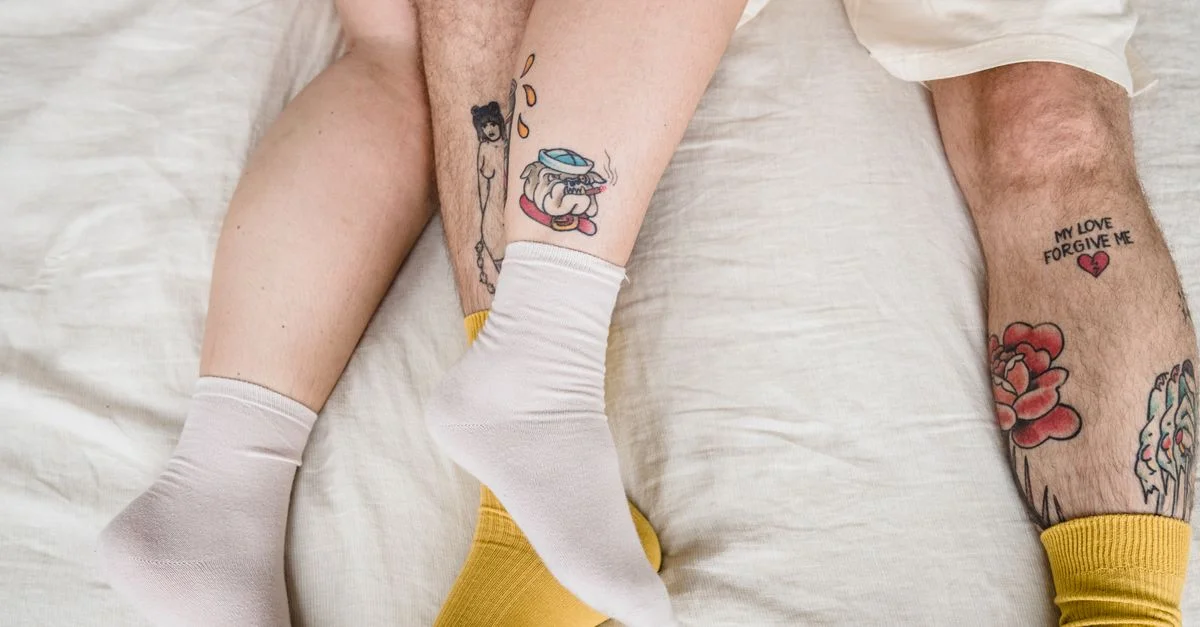 Vue de dessus des jambes tatouées d'un couple sur un lit, mettant en avant l'amour et le confort.