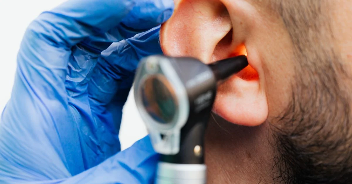 Gros plan d'un médecin utilisant un otoscope pour examiner l'oreille d'un patient dans un cadre clinique.