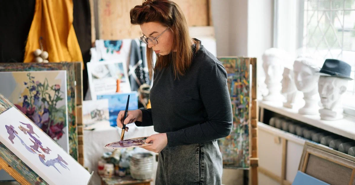 Une artiste femme peint sur une toile dans un studio lumineux et ensoleillé. Ambiance créative et concentrée.