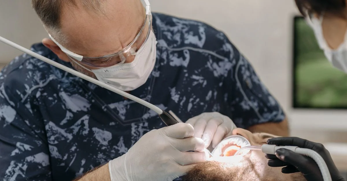Dentiste avec des instruments travaillant sur les dents d'un patient dans un cadre clinique.