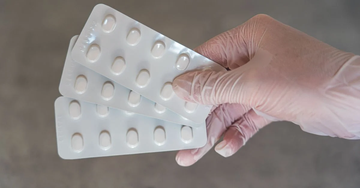 Main gantée tenant des plaquettes de médicaments, représentant les soins de santé et le traitement.