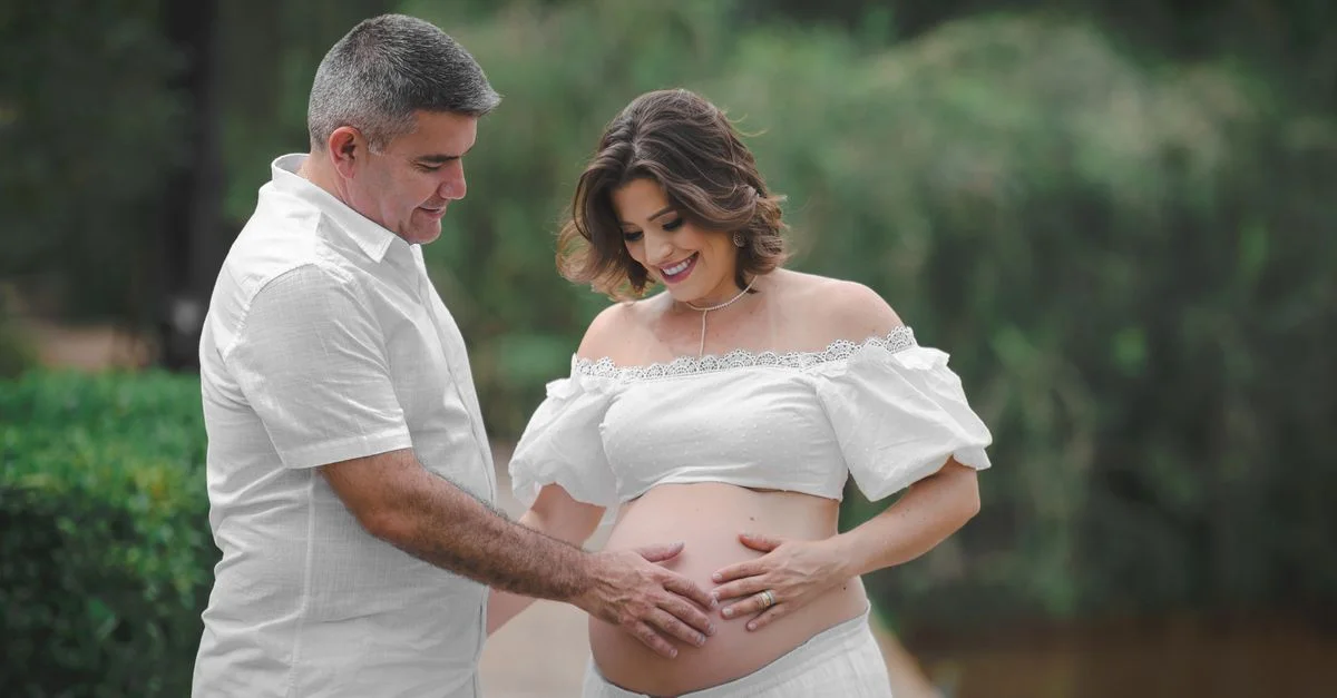 Couple enceinte en blanc partageant un moment tendre en plein air, symbolisant joie et amour.