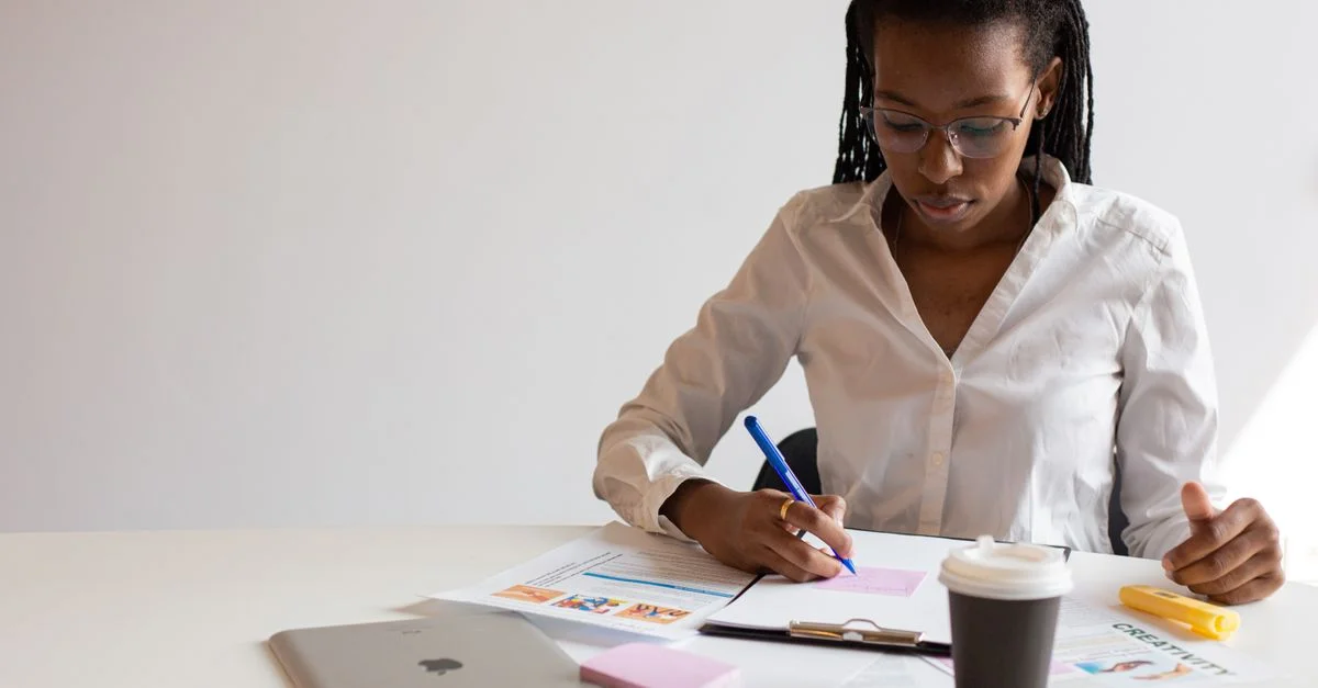 Femme professionnelle prenant des notes à son bureau avec des documents et un café.