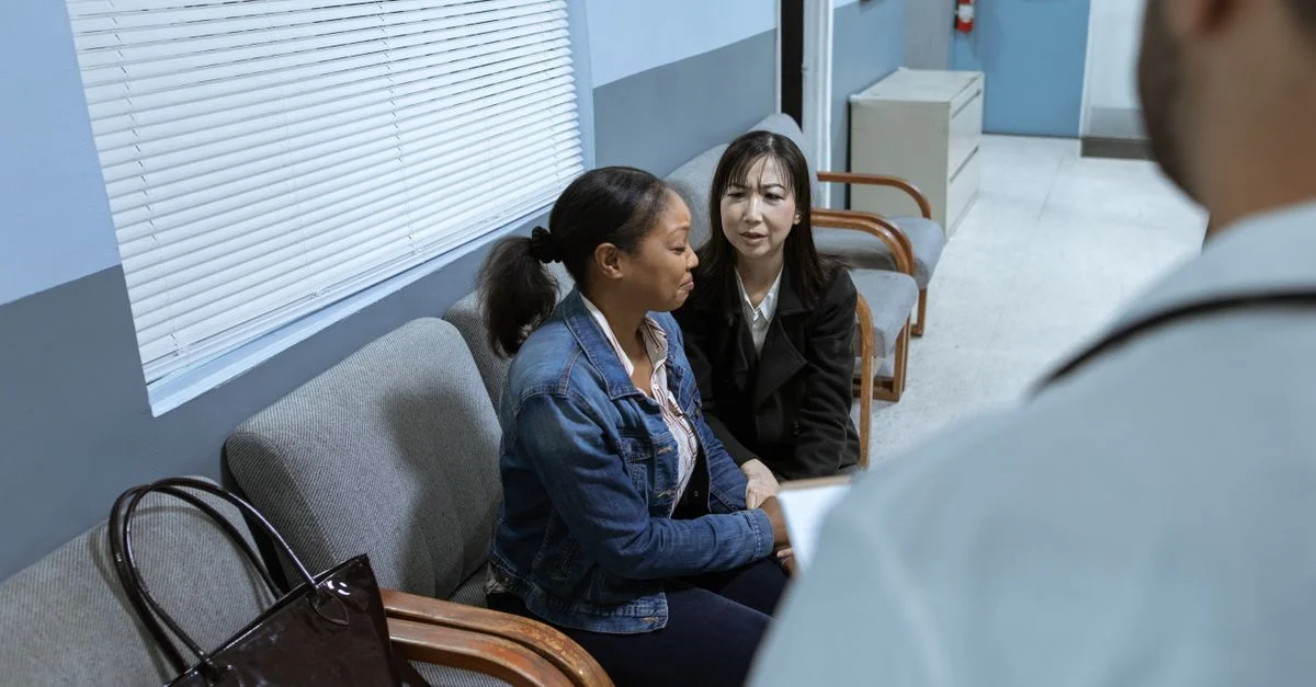 Deux femmes dans une salle d'attente de clinique discutent avec un médecin, illustrant l'interaction en santé.