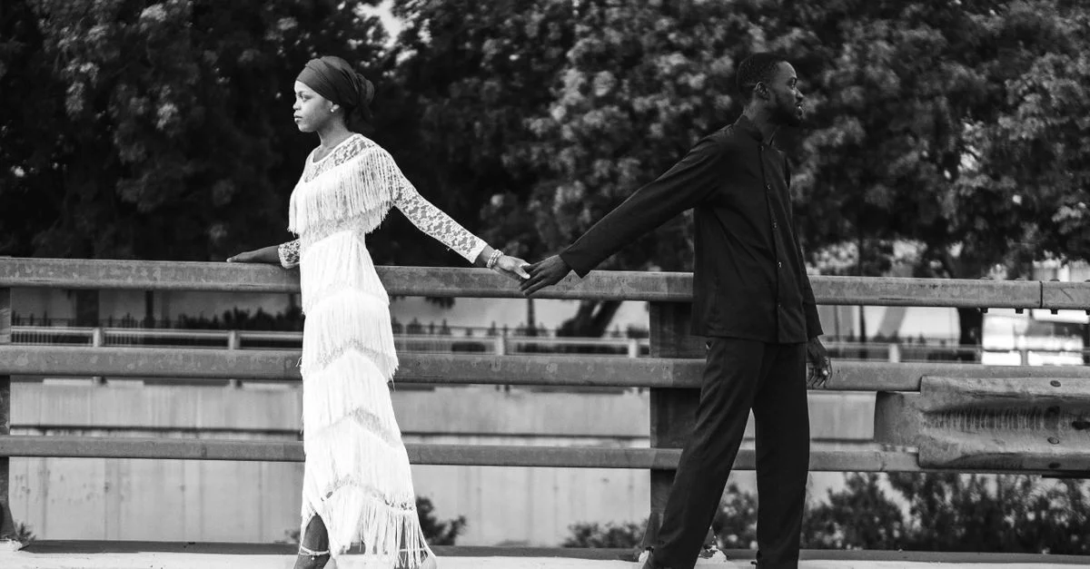 Élégante image en noir et blanc d'un couple se tenant la main sur un pont, illustrant le contraste et l'émotion.