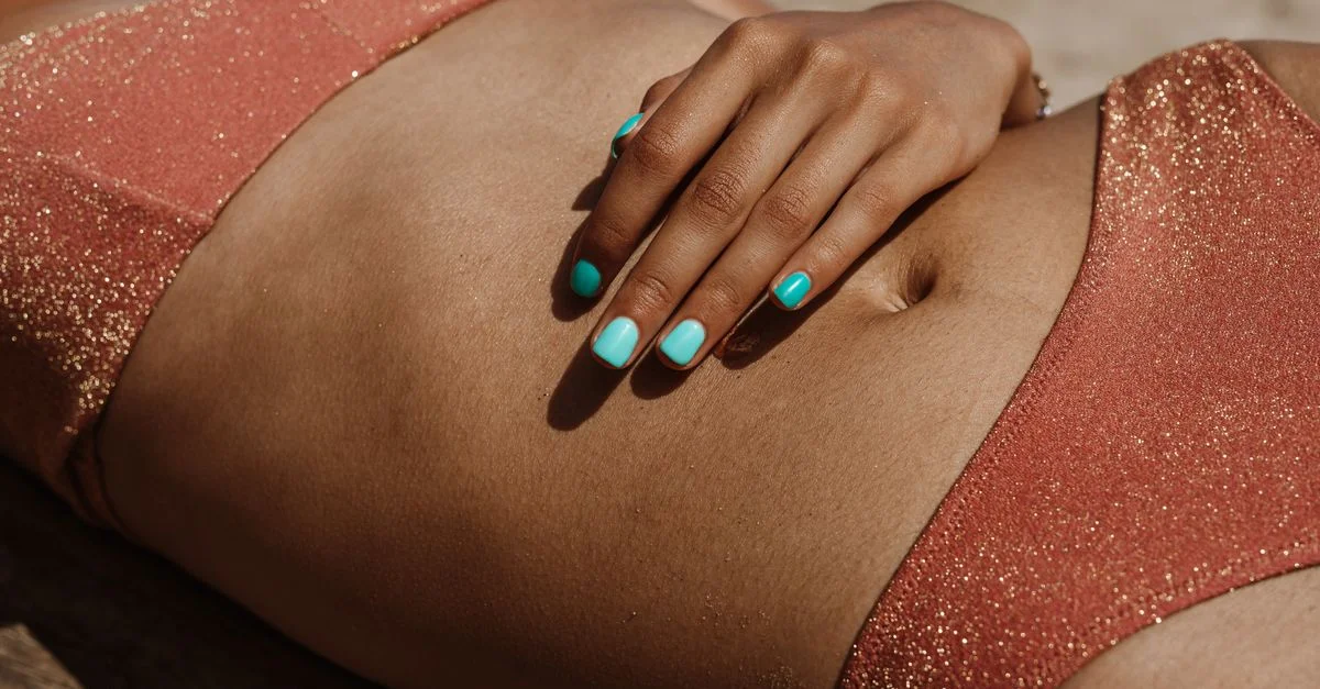 Un gros plan d'une femme allongée sur la plage dans un maillot de bain scintillant, mettant en valeur des ongles manucurés vibrants.