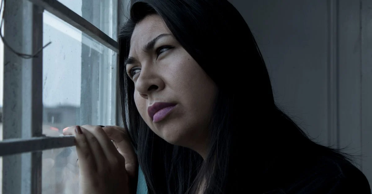 Une femme mélancolique regarde pensivement à travers une fenêtre, capturant une ambiance de contemplation.