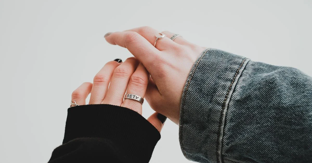Un gros plan de deux mains, portant des bagues en argent, se touchant doucement dans une veste en denim.