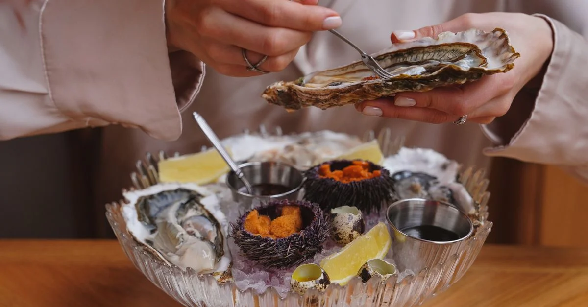 Gros plan sur une personne dégustant des huîtres fraîches et des oursins dans un cadre de restauration haut de gamme, mettant en valeur une cuisine de fruits de mer luxueuse.