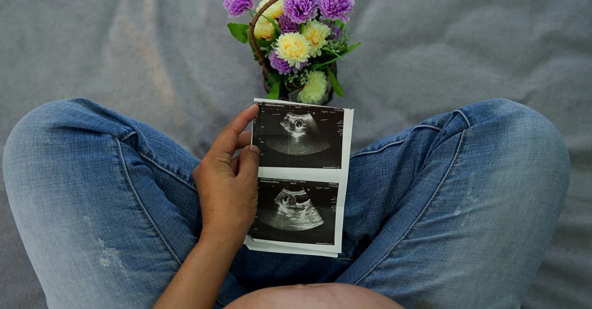 Une femme enceinte tenant des images d'échographie avec des fleurs, mettant en avant la joie maternelle.