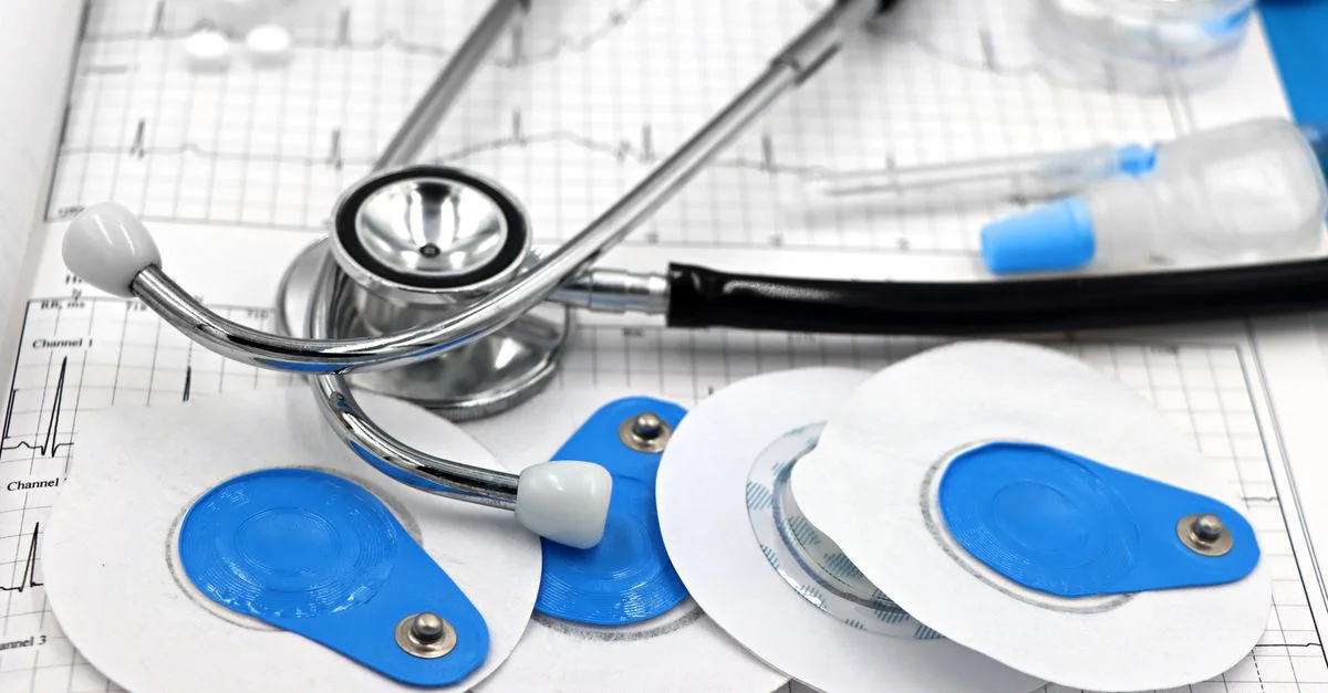 Gros plan sur des instruments médicaux, notamment des électrodes et un stéthoscope, figurant sur un tracé ECG.