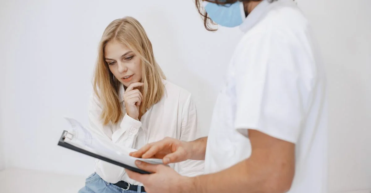 Un médecin en masque facial discute du diagnostic avec un patient dans un cadre clinique.