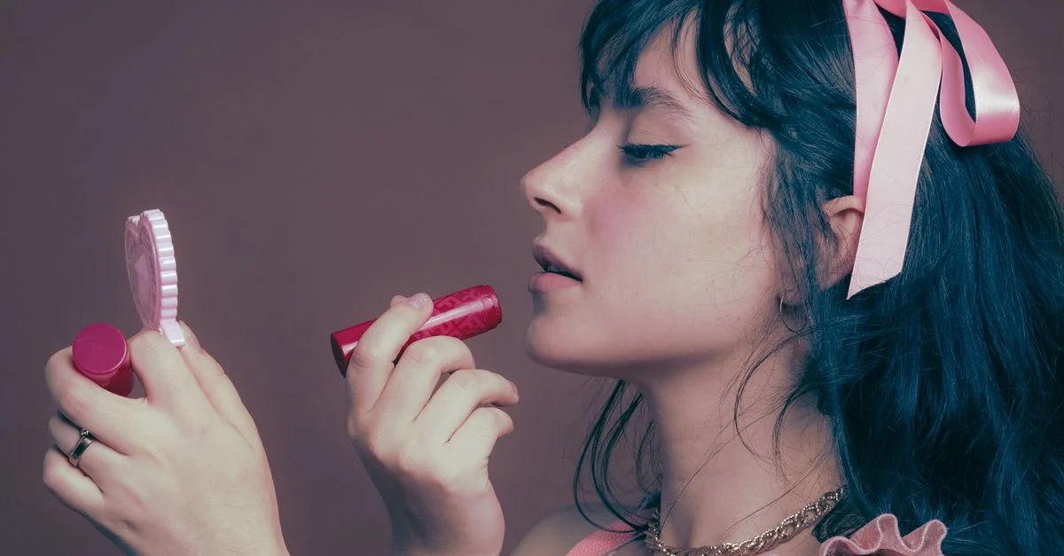 Portrait d'une jeune femme appliquant du rouge à lèvres, portant un nœud rose.