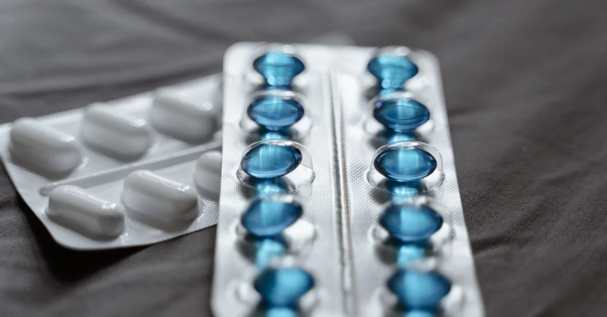 Vue détaillée de médicaments dans des plaquettes thermoformées montrant des capsules souples bleues et des comprimés blancs.