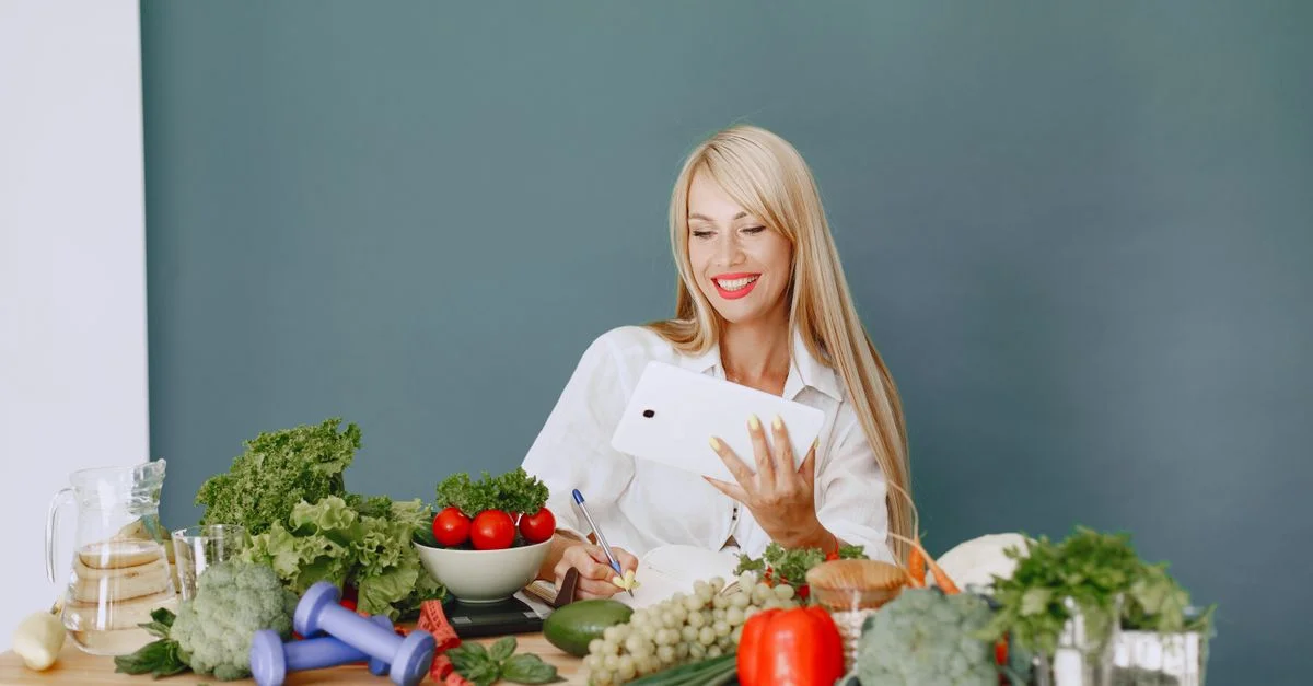 Femme utilisant une tablette entourée de légumes frais à une table, mettant en avant un mode de vie sain et la technologie.