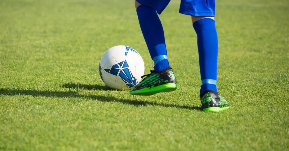 Gros plan d'un joueur de football dribblant un ballon sur un terrain vert vibrant au Portugal.