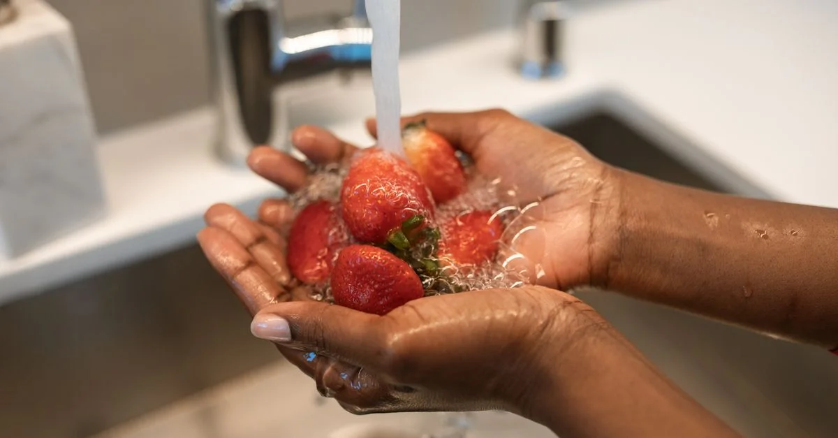 Gros plan sur des mains lavant des fraises sous l'eau courante dans un évier de cuisine, mettant l'accent sur la fraîcheur et la propreté.