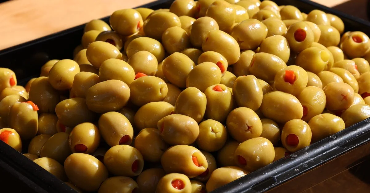 Gros plan sur des olives vertes fraîches et des piments dans un plateau noir.