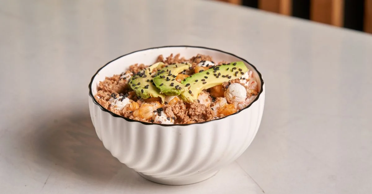 Bol de petit-déjeuner sain composé d'avocat, de granola et de graines de sésame dans un plat blanc.