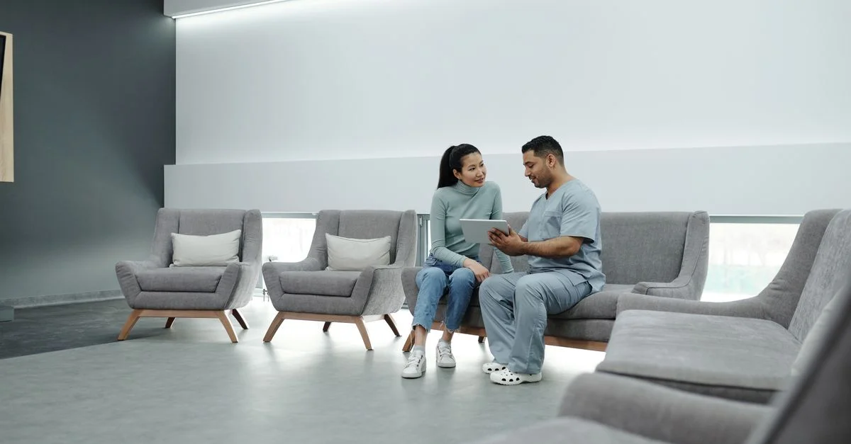 Un médecin en blouse consulté une patiente dans une salle d'attente moderne, utilisant une tablette.